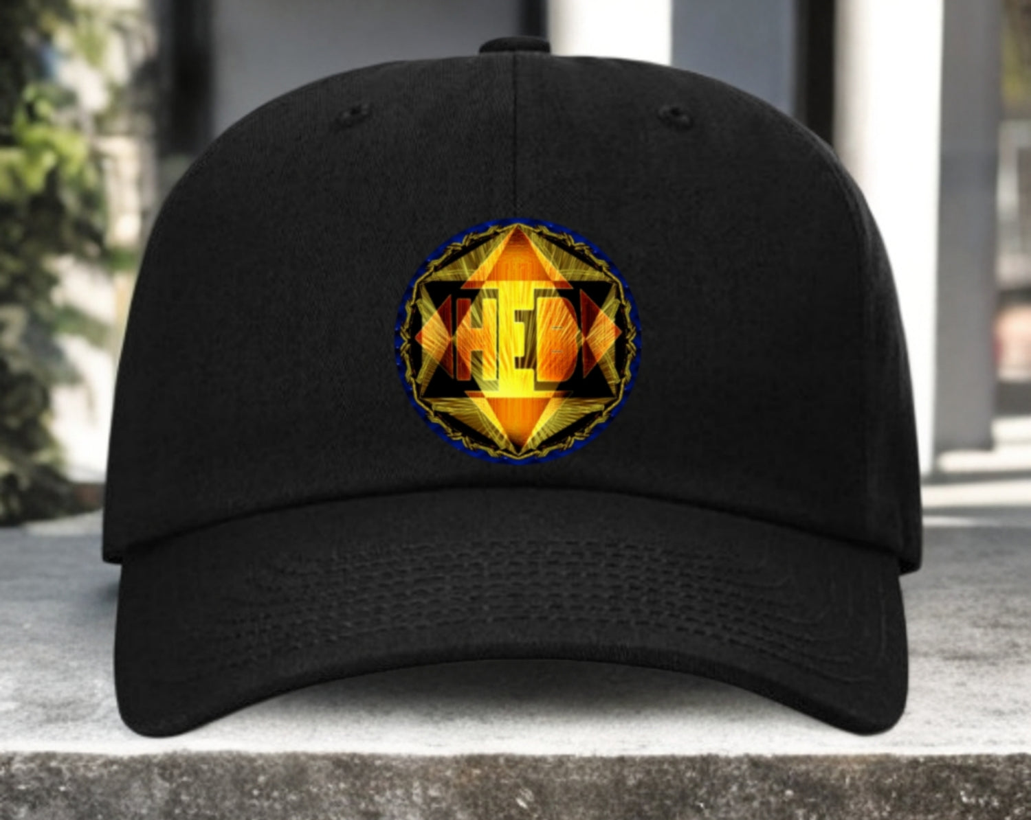 A front-facing black baseball cap featuring a circular, glowing gold and orange geometric emblem centered on the crown, resting on a stone surface.