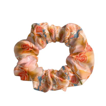 A high quality fabric hair scrunchie featuring the Apricot Bloom Essential print, showcasing detailed peach, cream, and coral roses on a muted blue background. 
