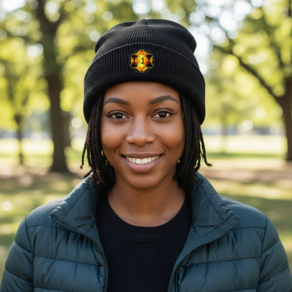A smiling woman with dreadlocks wearing a black beanie with a colorful logo and a green puffer jacket, outdoors with a blurred park background.