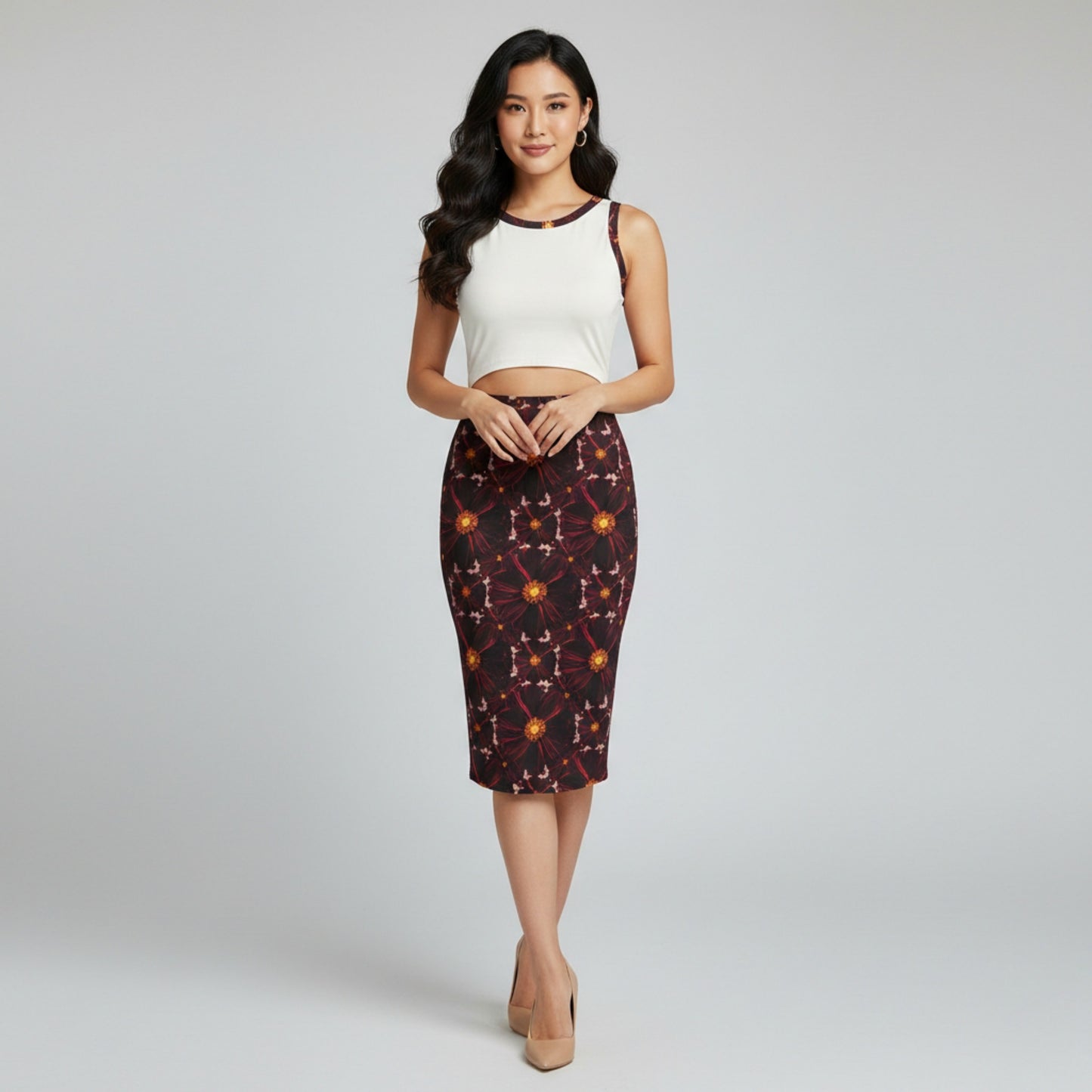 Woman wearing a white sleeveless crop top and dark floral midi skirt on a gray background. 