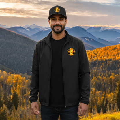 A smiling man wears a black zip-up jacket and matching baseball cap with a gold geometric log, standing against a scenic mountain and autumn forest backdrop.
