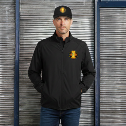 Man in a black jacket and baseball cap, both featuring a circular geometric gold logo, standing against a corrugated metal background. 