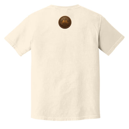 Flat lay of an ivory adult heavyweight tee showing the back with a circular gold "I AM" badge below the collar.