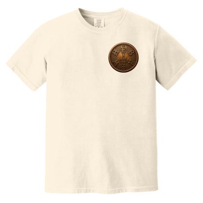 Flat lay of an ivory adult heavyweight tee showing the front with a circular gold "I AM" chest badge and "COMFORT COLORS" tag.
