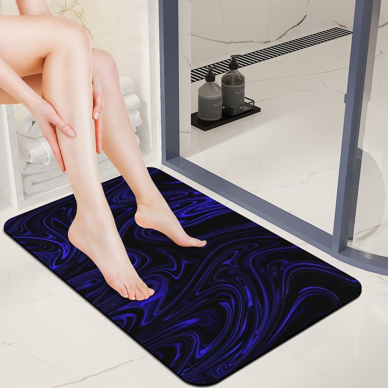 A person stepping onto the blue and black Flow (01-02) Cobalt bath mat in a modern white bathroom next to a glass shower door.