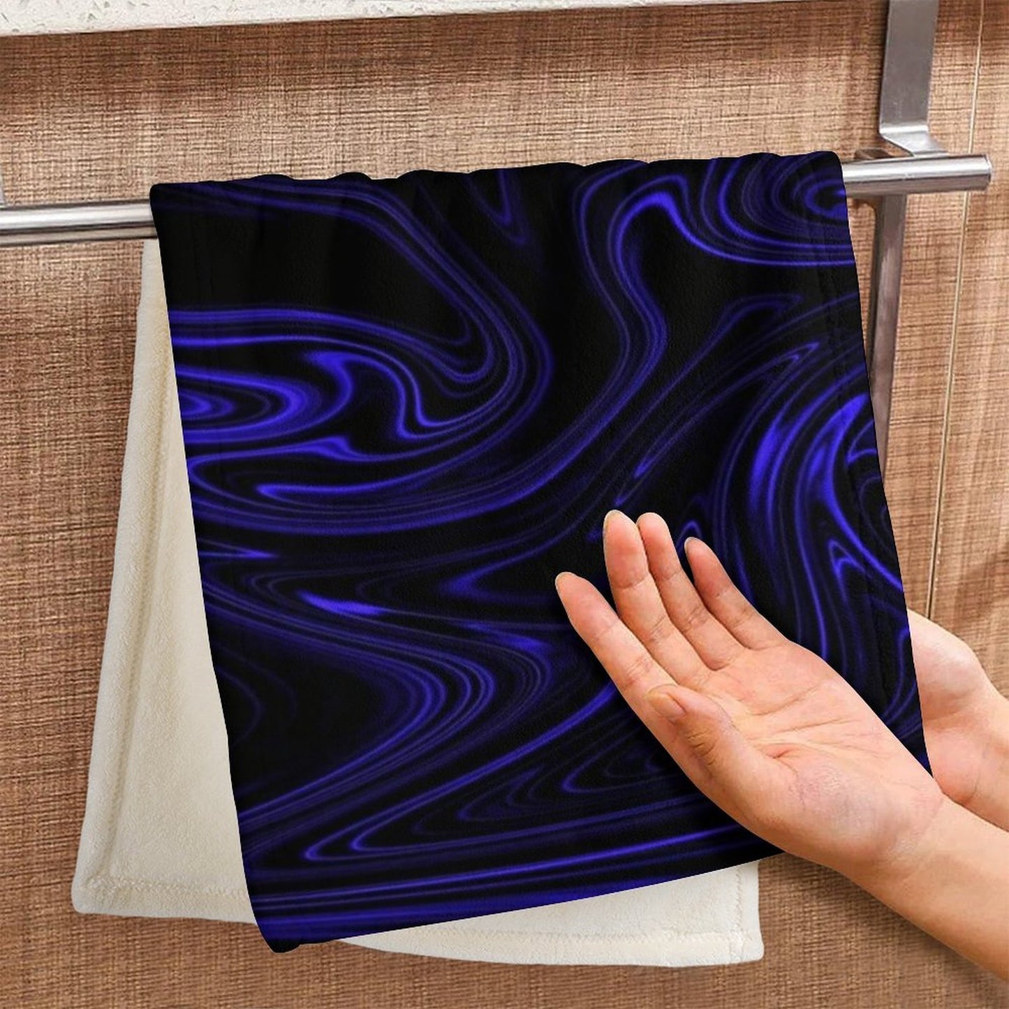 A hand reaching for a coral fleece hand towel hanging on a rack, featuring the Flow (01-02) Cobalt design with blue and black marble swirls.