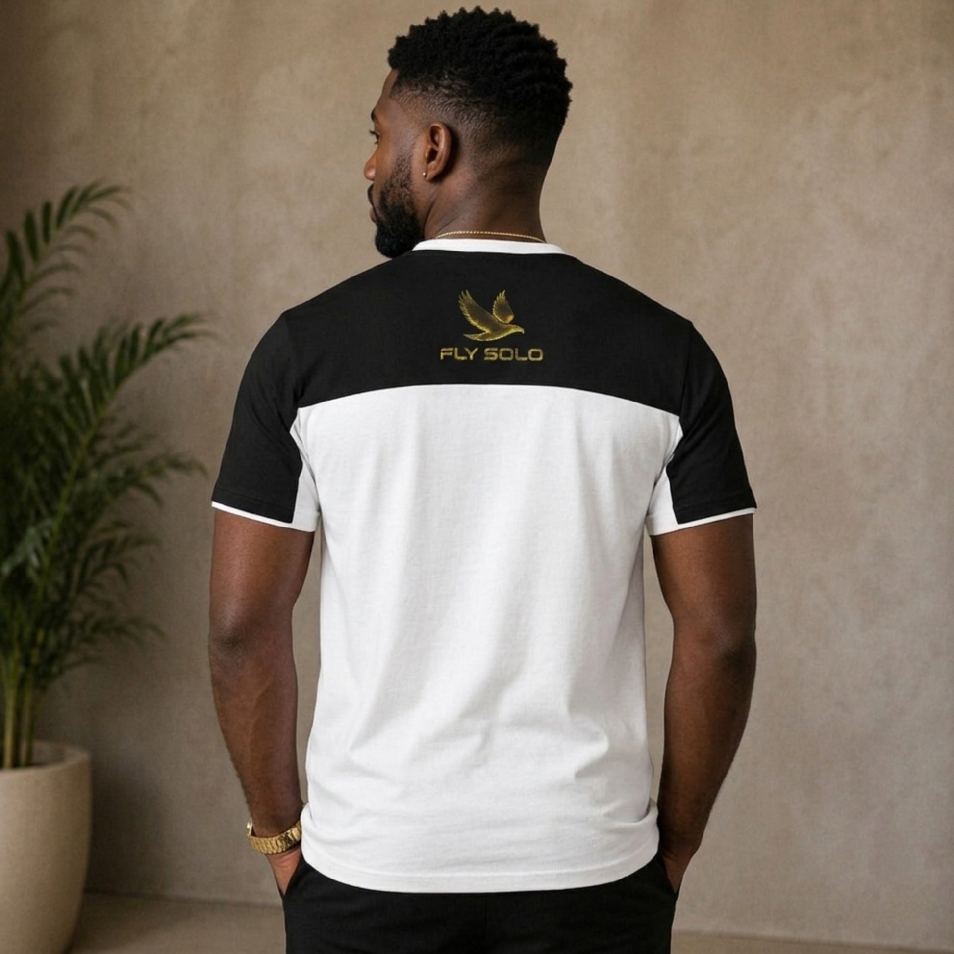 Back view of the Fly Solo split-panel tee worn by a man, showing the gold eagle logo and brand name centered on the black upper panel.