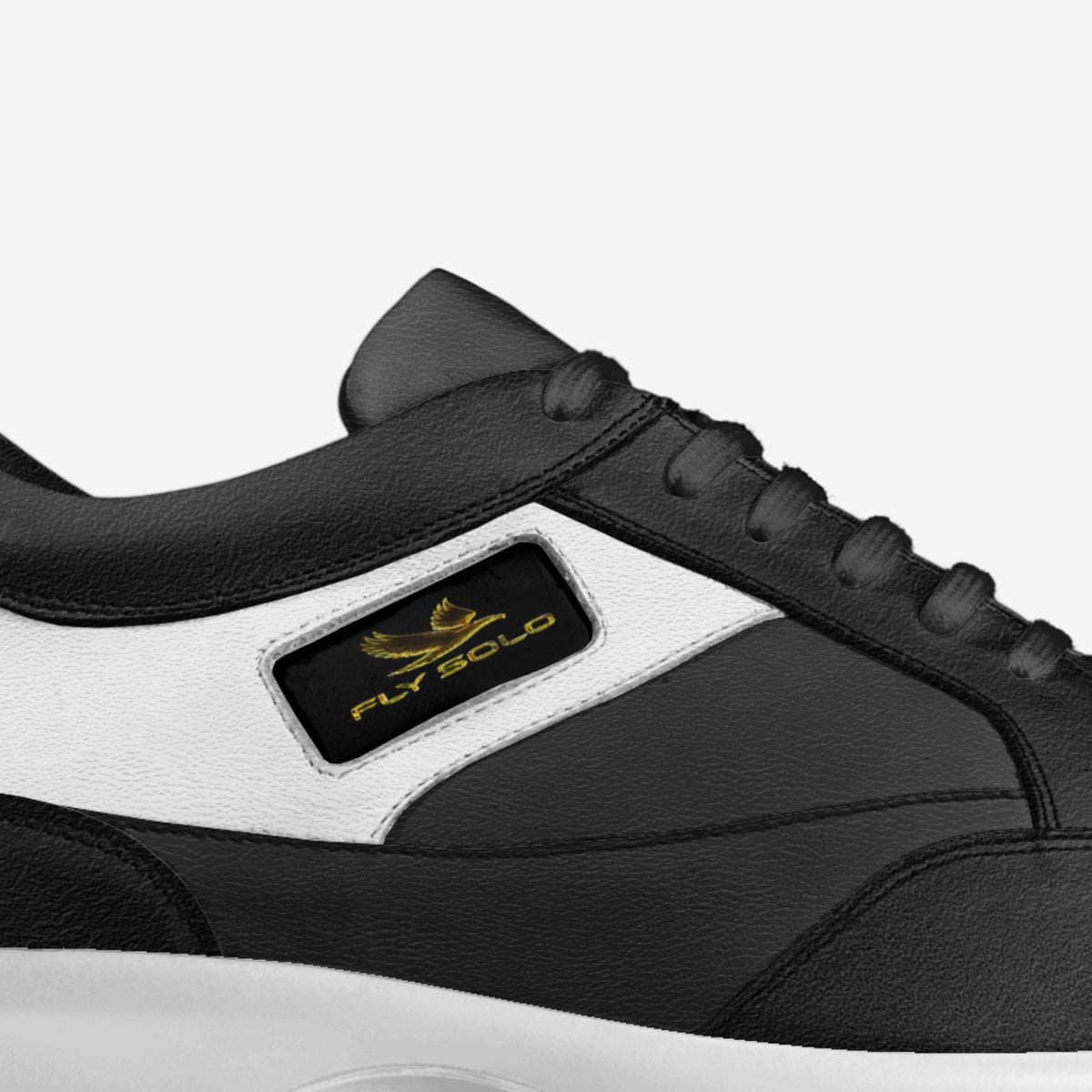 Close-up shot of the Fly Solo golden bird logo and brand name embossed on a black leather panel of the shoe.