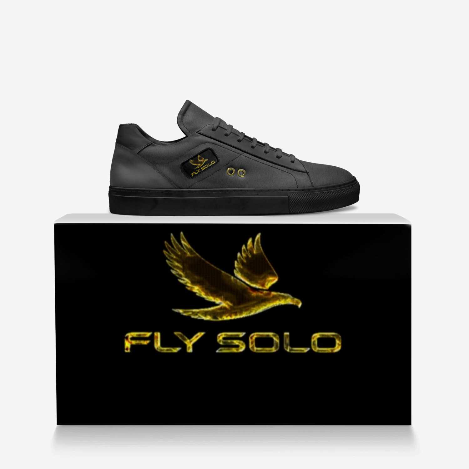 he all-black Fly Solo low-top sneaker is perched on a dark, branded shoebox. A large gold eagle logo is visible on the sneaker's tongue and the box.