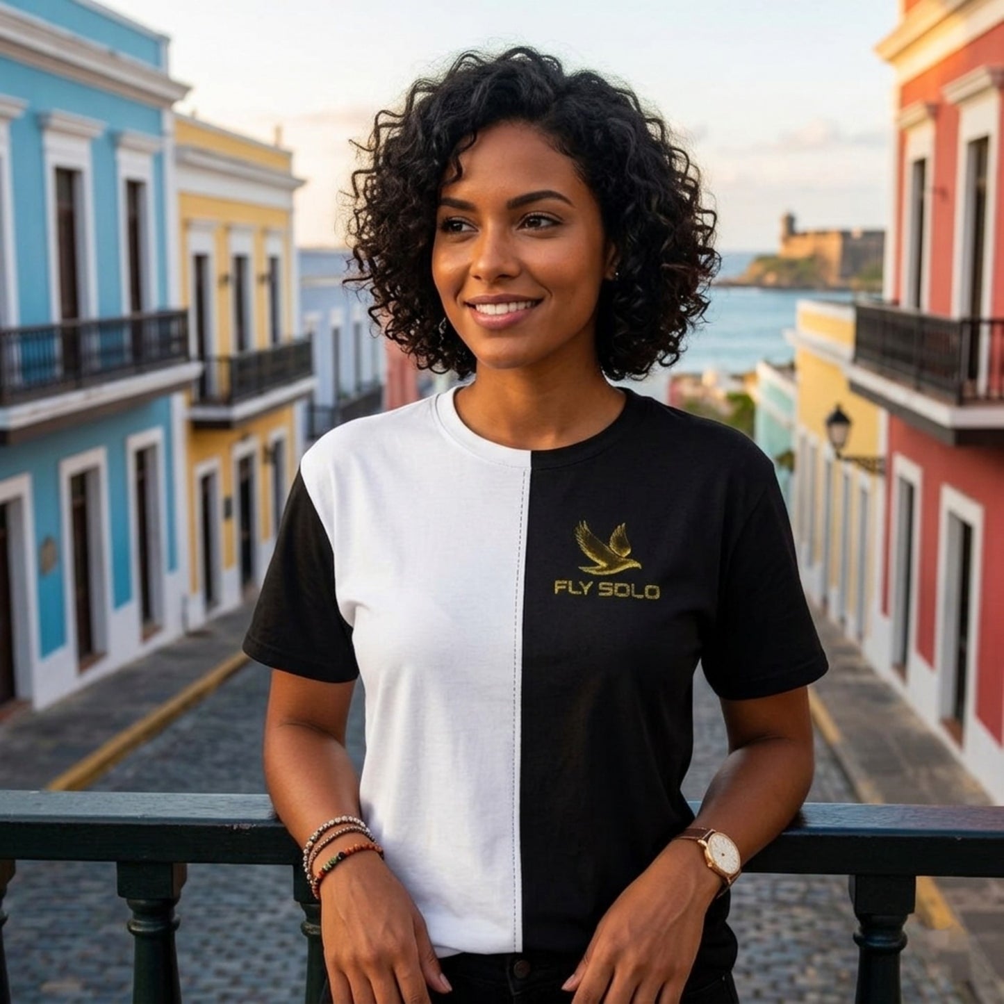 A woman wearing the Fly Solo split-panel tee, half white and half black, standing in a colorful historic street.