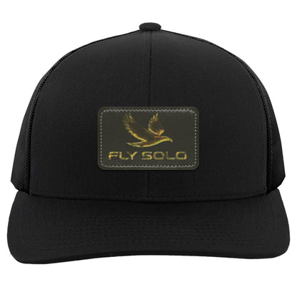 Clean front product shot of the solid black Fly Solo trucker hat with gold embossed branding.