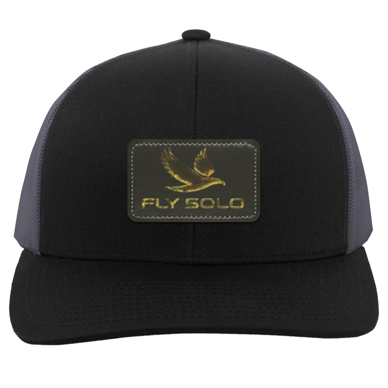 Front product shot of the black trucker hat with grey mesh panels and the signature gold brand logo.