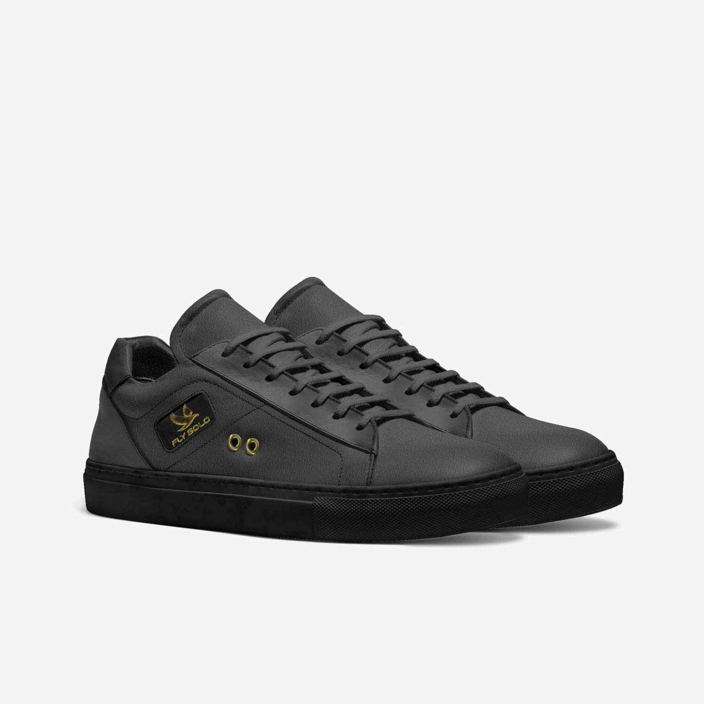 A pair of women's all-black Fly Solo sporty tennis style sneakers in dark grey leather, featuring a small gold eagle logo and brass lace eyelets.