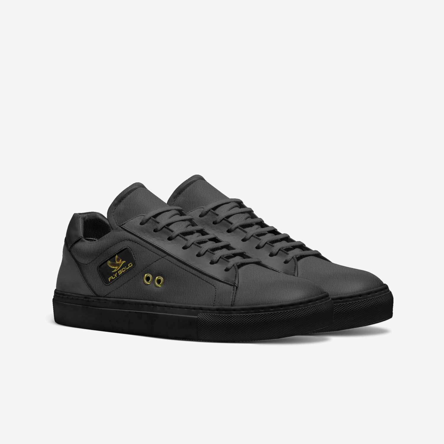 A pair of women's all-black Fly Solo sporty tennis style sneakers in dark grey leather, featuring a small gold eagle logo and brass lace eyelets.