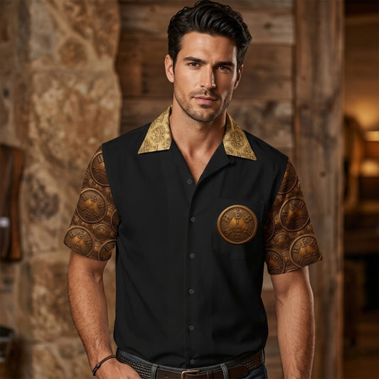 Full front view of the "I AM HEBREW: The Archive of Self" black short-sleeve Cuban collar shirt on a male model. The shirt features a right chest brass-look medallion with a braided rope edge.