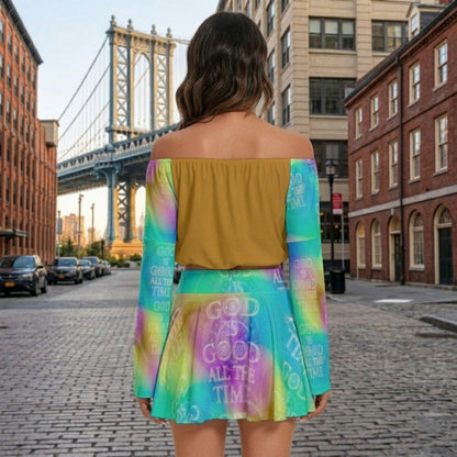 Back view of a woman on a city street wearing a mustard off-the-shoulder top and a colorful tie-dye skirt and sleeves with "God Is Good" text.