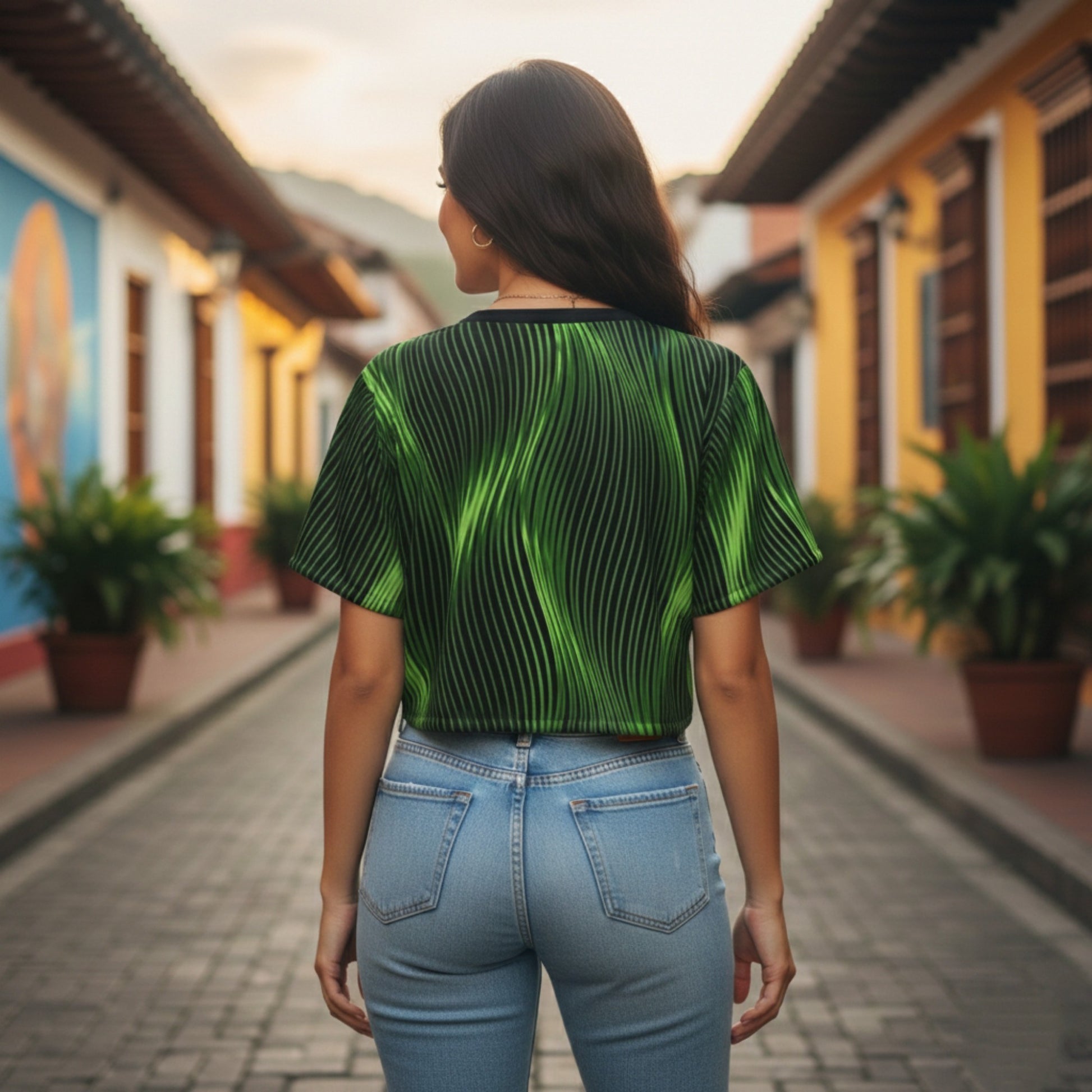 Back view of a woman in a green wavy-patterned crop top and blue jeans, standing on a cobblestone street lined with vibrant buildings.