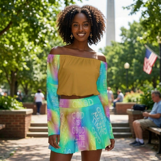 Front view of a woman in a park wearing a mustard off-the-shoulder top and a colorful "God Is Good All The Time" skirt and sleeves.