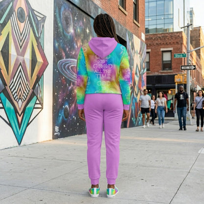 Back view of a woman standing in front of street mural wearing a purple tracksuit and a vibrant "God is Good All the Time" tie-dye hoodie.