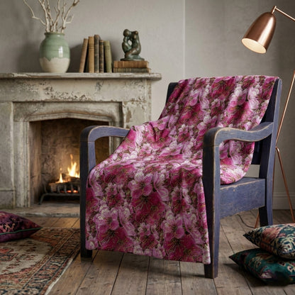 Crushed velvet blanket with a vibrant pink and white cherry blossom floral pattern, shown draped over a wooden armchair.
