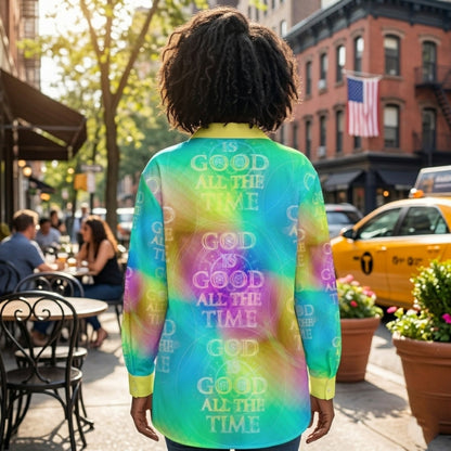 Rear view of a woman on a city street wearing a colorful, patterned long-sleeve shirt with the words "GOD IS GOOD ALL THE TIME" printed across the back.