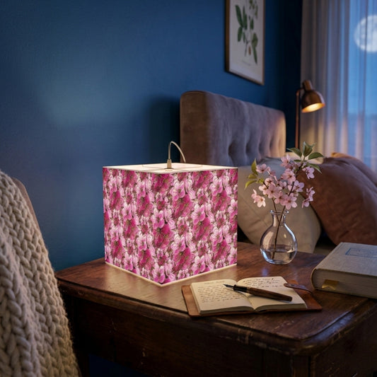 Cozy bedroom nightstand with a square table lamp in a pink floral print, next to a journal, fountain pen, and a small vase of pink blossoms.