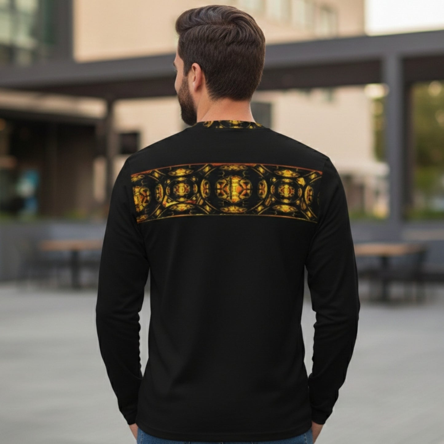 Rear view of a man in a black long-sleeve shirt featuring a gold ornate pattern band across the shoulders, standing in an outdoor urban setting.