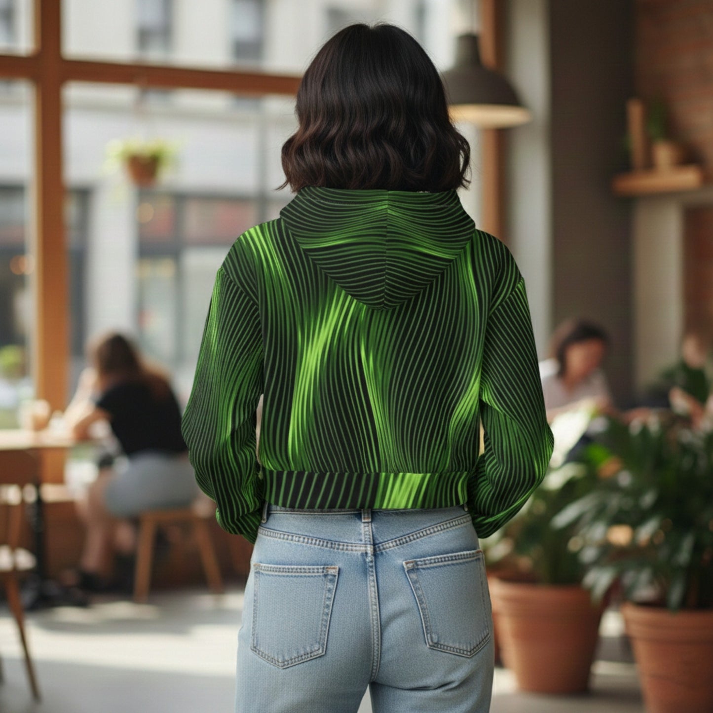 Rear view of a woman in a cafe wearing a cropped hoodie with a vibrant green and black wavy pinstripe pattern and light-wash jeans.