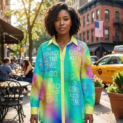 A woman standing on a busy New York City sidewalk wearing a bright, multi-colored button-down shirt with the text "GOD IS GOOD ALL THE TIME" repeated throughout.