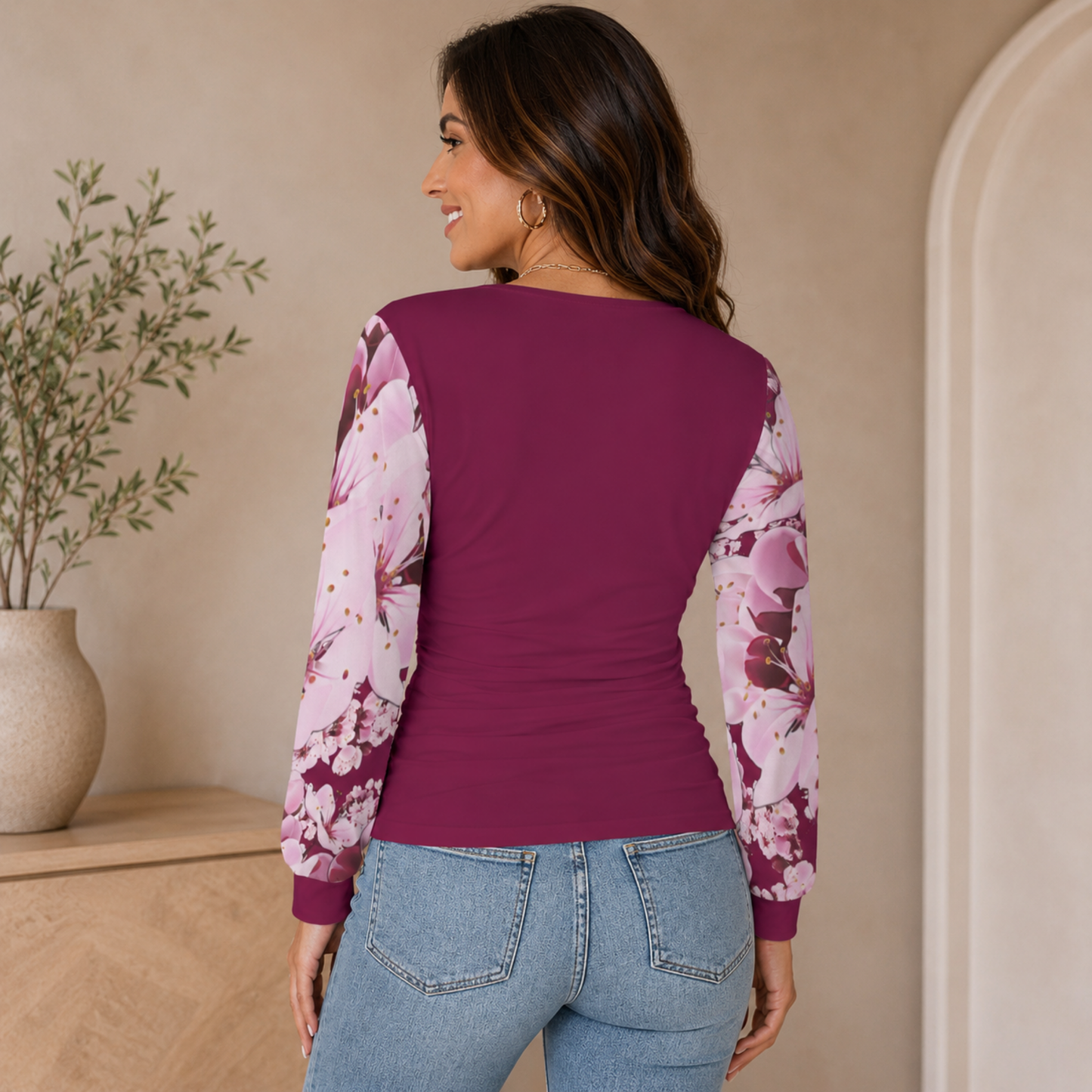 Full back view of a woman wearing a solid plum knit blouse with contrast pink sakura floral print sleeves, paired with denim jeans.