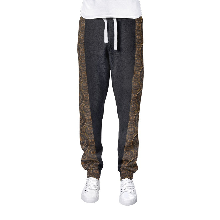 Isolated front view of men's dark grey joggers featuring structured white drawstrings and ornate antiqued bronze medallion patterns on the side panels.