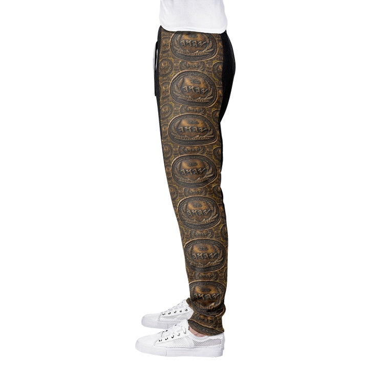 Detailed side profile of joggers showcasing a repeating antiqued bronze coin pattern with Paleo-Hebrew script text along the outer leg.