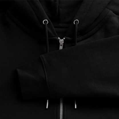 Macro view of a black organic zip hoodie fabric, showcasing the silver metallic zipper track, drawstrings with silver tips, and ribbed sleeve cuff.