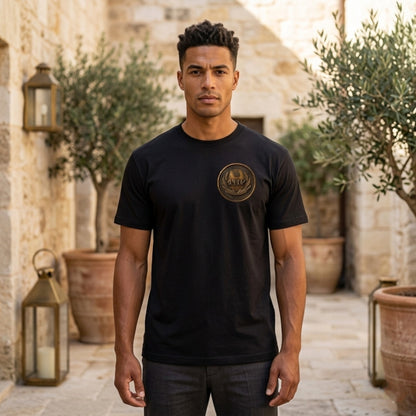Front view of a man in a black oversized heavyweight t-shirt with a circular antiqued bronze medallion emblem on the chest.