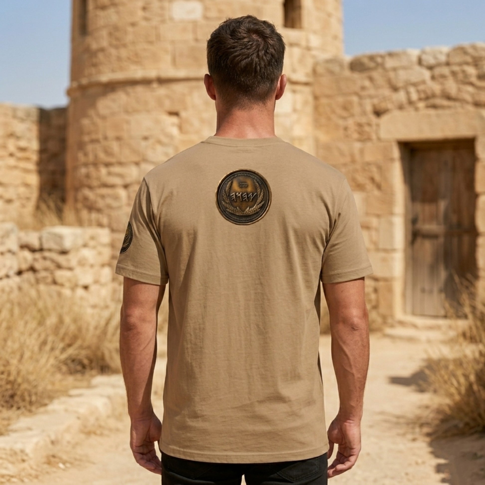 Back view of a tan oversized heavyweight t-shirt featuring a large, central circular antiqued bronze medallion emblem with Paleo-Hebrew typography.