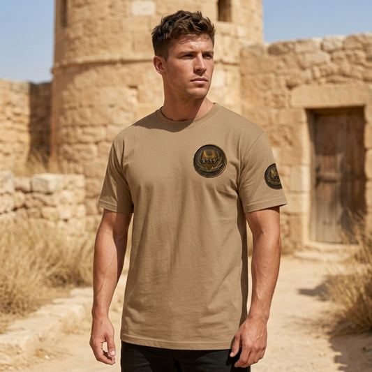 Front view of a man in a tan oversized heavyweight t-shirt featuring a circular antiqued bronze medallion emblem with Paleo-Hebrew text.