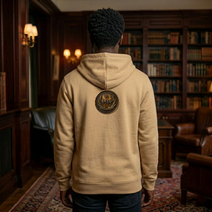 Back view of a tan organic zip hoodie featuring a centered circular antiqued bronze symbolic emblem, set against a library backdrop.