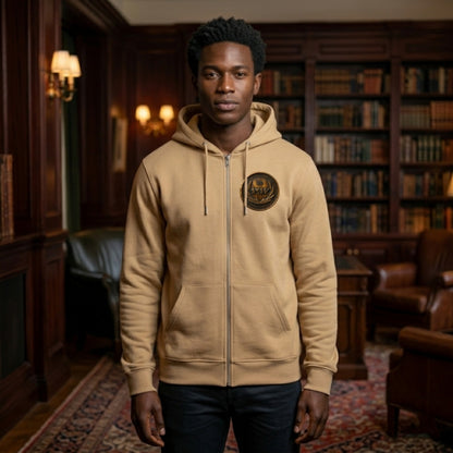Front view of a man in a classic library setting wearing a tan organic zip hoodie with a circular antiqued bronze medallion patch.