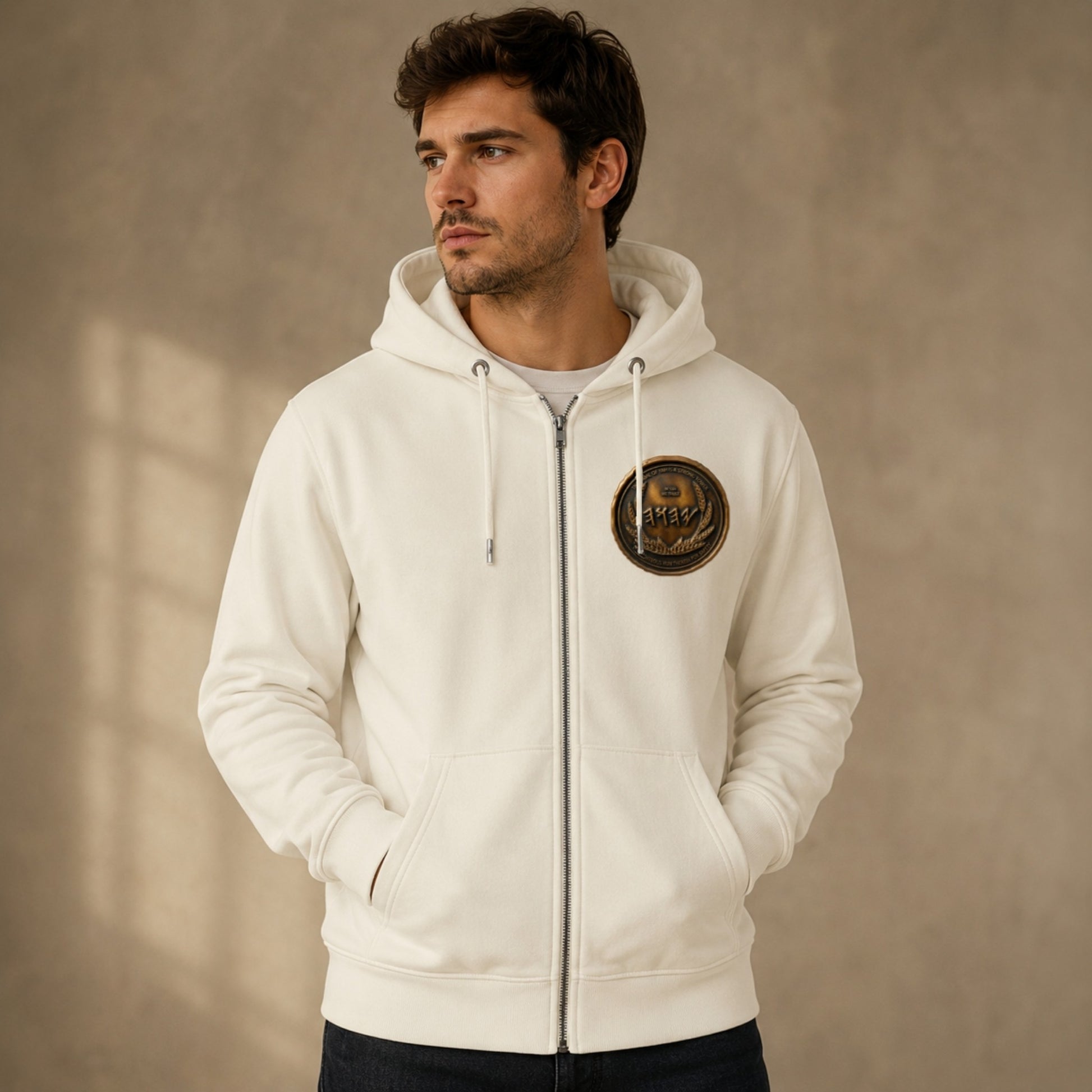 Front view of a man looking to the side wearing a white organic zip hoodie highlighted by a contrasting circular antiqued bronze chest emblem.