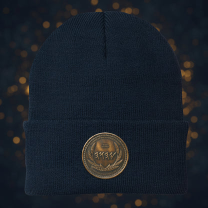 Detailed view of the antiqued bronze symbolic script medallion on a cuffed navy blue knit beanie.