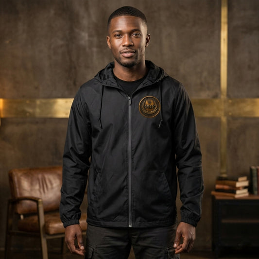 Front view of a man wearing a black windbreaker featuring a circular antiqued bronze medallion emblem with Paleo-Hebrew script on the left chest.