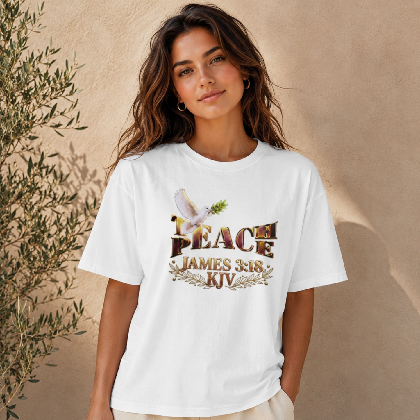 A woman modeling the white Teach Peace James 3:18 oversized t-shirt against a textured wall background.